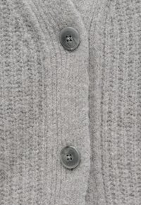 Svetle šedý pletený kardigan s žebrovanou texturou a kulatým tmavě šedým knoflíkem se čtyřmi dírkami.
