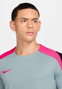 Maglietta sportiva a maniche corte in tessuto grigio chiaro, con accenti rosa sulle spalle. Superficie texture con logo Nike in rosa.