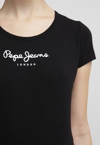 Camiseta de algodón negra con mangas cortas, que presenta un logo blanco que dice "Pepe Jeans London" en el pecho. Diseño de cuello redondo.