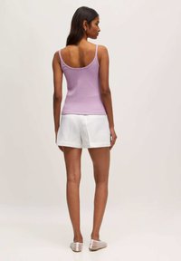 Lila tanktop met dunne bandjes, aansluitend ontwerp, gecombineerd met witte op maat gemaakte shorts, platte sandalen en stijlvol haar. Glad stoftextuur.