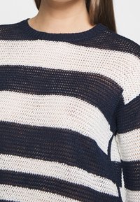 Navy and white striped knit sweater with a round neckline, textured open weave, and long sleeves. Features contrasting horizontal stripes.