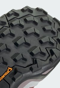 Svart gummisåle med multidireksjonale klumper for grep. Har et mønstret tekstur og en oransje Continental-logo på siden.