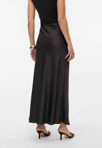 Jupe maxi en satin noir avec une texture lisse, présentant une taille cintrée et un design fluide qui tombe jusqu'au milieu du mollet, associée à des sandales à talons marron.