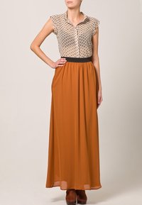 Blusa de lunares en beige, diseño de botones; combinada con una falda larga y fluida naranja con cintura elástica y bolsillos.