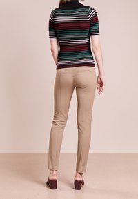 Gestreepte trui met korte mouwen in donkerrood, groen en zwart, gecombineerd met beige slim-fit broeken en donker blokhakken mules. Achteraanzicht weergegeven.