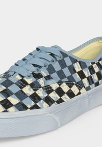 Κλασικό παπούτσι Vans με μοτίβο καρό σε μπλε και μαύρο χρώμα και λεπτομέρειες με πιτσιλιές μπογιάς, ανοιχτό μπλε κορδόνια και λευκή λάστιχη σόλα.