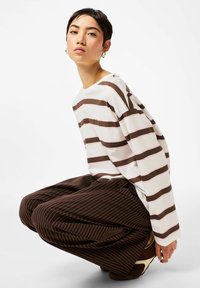 Valge ja pruun triibuline pikkade varrukatega särk, mis on kombineeritud pruunide pinstripe-pükstega, omades lõdvestunud istuvust ja pehmet tekstuuri.