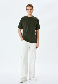 Mörkgrön bomulls t-shirt med korta ärmar, rund halslinning och avslappnad passform, tillsammans med vita cargobyxor med sidofickor.