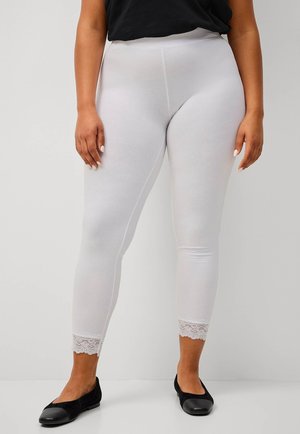 Witte leggings van rekbaar materiaal, met een kantaccent aan de zoom, gecombineerd met zwarte flats. Zachte textuur overal.