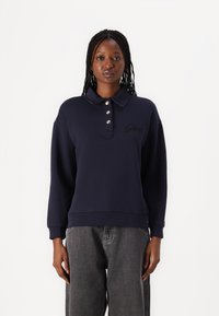 Marineblauwe pullover met een kraag en een drie knopen sluiting, met een klein geborduurd logo op de borst. Zacht materiaal en een comfortabele pasvorm.