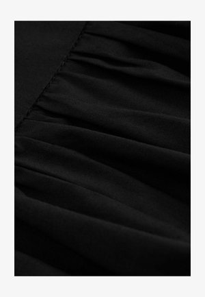 Mustaa kangasta, jossa on poimutettu rakenne, pehmeä ja sileä materiaali sekä hienovarainen kiilto. Yksityiskohtaiset ompeleet reunoilla.