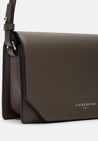Dunkelolivgrüne Lederhandtasche mit einem Klappendesign, das kontrastierende Nähte und ein silbernes Logo auf der Vorderseite aufweist. Verstellbarer Riemen inklusive.