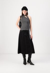 Fekete farmer szoknya látható varrással, csíkos halter top-pal párosítva, valamint egy fekete kötött sapkával. A modellen fekete, hegyes orrú csizmák vannak.