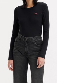 Czarna koszulka z długim rękawem i okrągłym dekoltem z czerwonym logo Levi's na piersi, zestawiona z wysokim stanem czarnymi jeansami z delikatnym przetarciem.