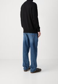 Sweat-shirt noir avec ourlet côtelé, associé à un jean en denim bleu ample. La tenue présente une coupe décontractée et un design simple.