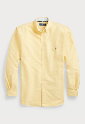 Camisa amarilla de botonadura frontal, hecha de algodón, con mangas largas, un cuello y un pequeño logo bordado en el lado izquierdo del pecho.