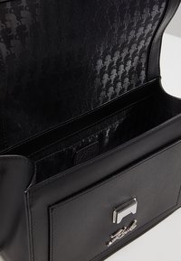 Borsa a tracolla in pelle nera con forma strutturata, accessori in argento e interno in tessuto a fantasia. Presenta una tasca frontale e un'etichetta con il marchio.