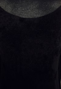Gros plan d'un tissu noir à col rond avec un motif tricoté fin et texturé et une surface douce et duveteuse.