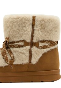 Brune ruskindsstøvler med en cremefarvet faux fur kant, dekorative brune mønstrede snørebånd og en sidelukning med lynlås. Flad, tekstureret sål.