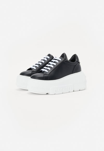 Black leather sneakers with white laces and a thick white rubber sole. Features a smooth texture and rounded toe design.