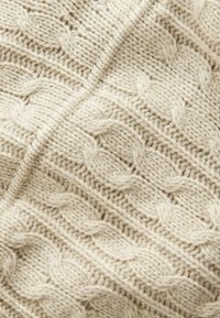 Off-white gestrickter Stoff mit einem strukturierten Kabelmuster, das sich durch markante erhabene Maschen und ein weiches, gemütliches Erscheinungsbild auszeichnet.