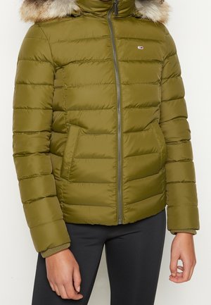 Olijfgroene gewatteerde pufferjas met een met bont afgezoomde capuchon, een ritssluiting aan de voorkant, zijzakken, gedragen met een zwarte broek.