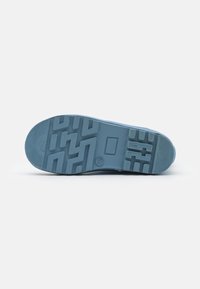 Semelle de sneaker bleu clair avec une surface en caoutchouc texturé, présentant un motif en zigzag et un emblème rectangulaire. Le numéro "29" est embossé.