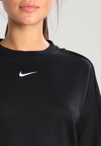 Czarna bluza z miękkiego materiału, z okrągłym dekoltem i małym białym logo Nike na piersi. Gładka tekstura z minimalnym wzornictwem.