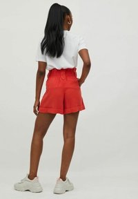 Pantalones cortos rojos con cintura fruncida y piernas anchas, con dobladillo doblado. Combinados con una camiseta blanca y zapatillas de color claro.