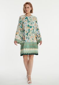 Robe à motif floral avec un fond teal et des fleurs pêches et crème, manches amples et ourlet incurvé accentué par des rayures.