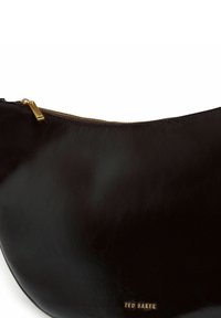 Glänzende schwarze Lederhülle mit goldfarbenem Reißverschluss und kleinem goldfarbenem "Ted Baker"-Logo nahe dem unteren Rand.