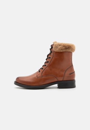 Botas de tobillo de cuero marrón con un collar de piel sintética, diseño de cordones, punta redonda y un tacón bajo de bloque. Textura suave con sutilezas en los detalles de costura.
