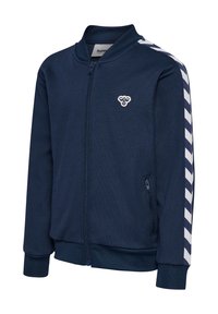 Giacca con zip color blu navy, con polsini e colletto a costine. Strisce laterali bianche presentano un motivo a chevron. Piccolo logo sul petto.