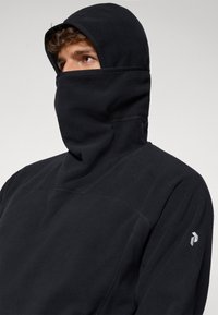 Pull en polaire noir avec un col à capuche haut. Il présente une texture lisse, un design simple et un accent de logo sur l'épaule gauche.