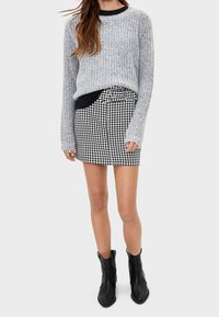 Šedý pletený svetr s kulatým výstřihem a dlouhými rukávy, doplněný černobílou kostkovanou mini sukni a černými kotníkovými botami.