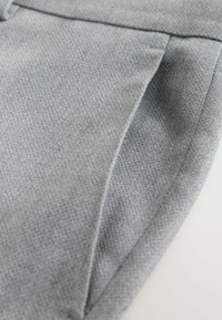 Grijs gestructureerde stof met een subtiel geweven patroon. Voorzien van een zijnaadzak en nette randen, met een gladde afwerking.