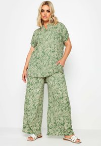 Blusa a fantasia paisley verde con pantaloni larghi coordinati. Tessuto leggero, maniche corte e due tasche laterali. Sandali bianchi completano il look.