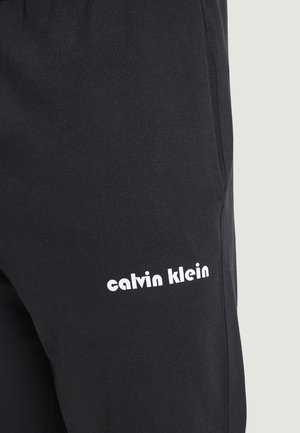 Pantaloni sportivi neri realizzati in un morbido tessuto, con il logo bianco "calvin klein" sul lato, dalla texture liscia e dal design slim.