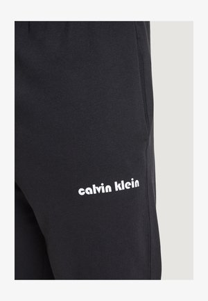 Schwarze Sweatpants aus weichem Stoff, mit einem weißen "calvin klein" Logo an der Seite, glatter Textur und schlankem Design.