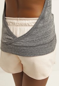 Personne portant un short beige clair et un haut gris légèrement relevé pour révéler la taille du short.
