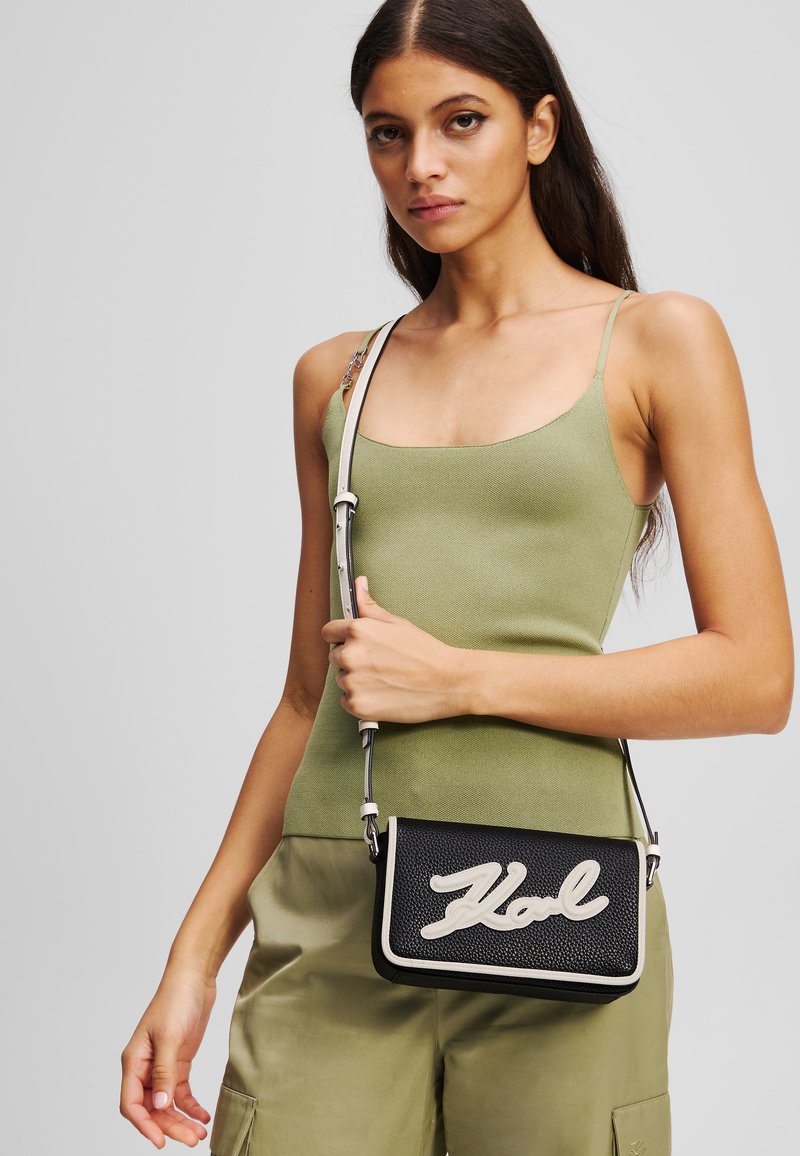 Borsa a tracolla nera con texture e scritta bianca "Hol." Dotata di una tracolla rimovibile e di forma rettangolare, progettata per un uso casual.
