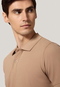 Beżowa koszulka polo z teksturowanej tkaniny, klasycznym kołnierzykiem i pojedynczym guzikiem przy szyi. Krótkie rękawy, dopasowany krój.