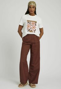 T-shirt blanc avec imprimé floral en rose et marron, assorti à un pantalon large taille haute couleur rouille et des sandales tressées couleur tan.