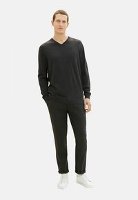 Black, long-sleeve V-neck sweater paired with dark trousers and white sneakers. The fabric appears smooth, offering a casual look.