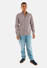 Chemise à manches longues pour hommes avec un motif rouge et blanc, à boutons, associée à un jean bleu clair et des baskets noires avec des accents marron.