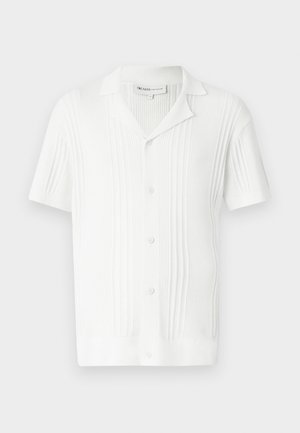 Camicetta bianca a maniche corte con texture a coste, chiusura con bottoni e colletto. Presenta righe verticali per un tocco di dettaglio.