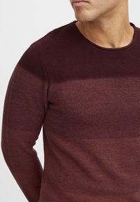 Maroon knitted sweater featuring a textured pattern, a round neckline, and long sleeves with a gradual color variation.