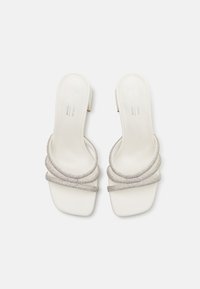 Mules à bout ouvert en cuir vegan blanc, dotées d'un talon carré et de brides en strass en ton argent avec une texture lisse.