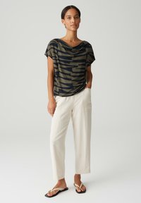 Olijfgroene en zwarte gestreepte losse T-shirt met een gedrapeerde halslijn, gecombineerd met crème kleurige rechtliggende broeken en flip-flop sandalen.