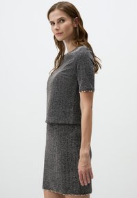 Ensemble deux pièces gris comprenant un haut à manches courtes et une jupe ajustée, confectionné dans un tissu texturé avec des accents de perles sur les bords des manches.